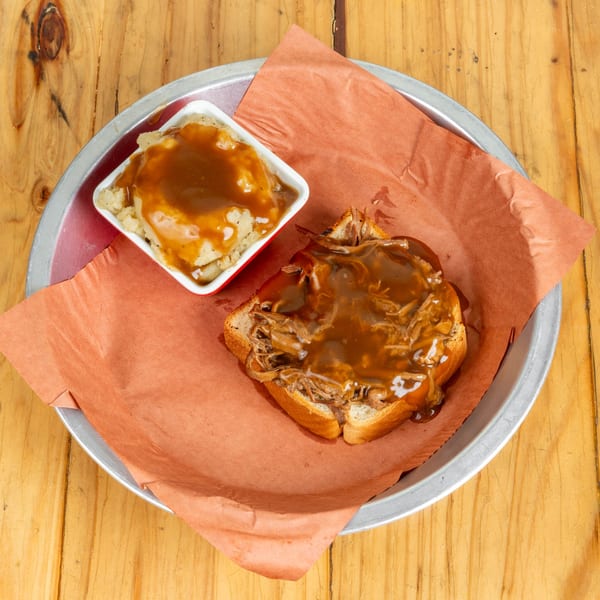 Open-faced pulled pork sandwich with gravy and a side of mashed potatoes on a metal tray.