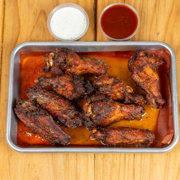 A metal tray of crispy, seasoned chicken wings with two dipping sauces on a wooden table.