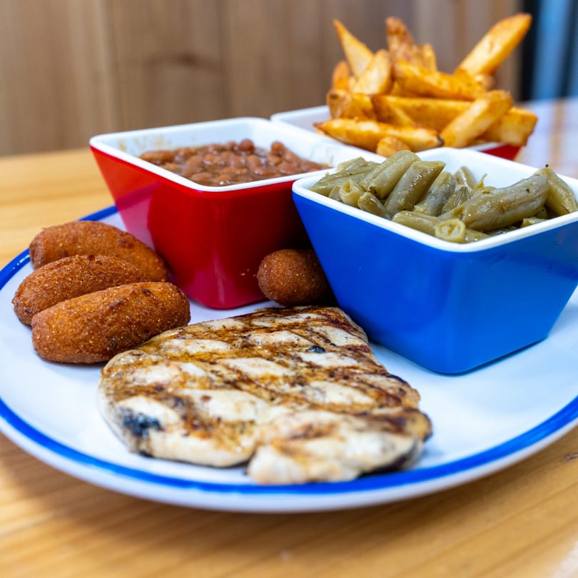 Grilled chicken, hush puppies, baked beans, green beans, and fries on a white plate.