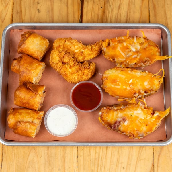 Appetizer platter with fried chicken, loaded potato skins, egg rolls, ranch, and barbecue sauce.