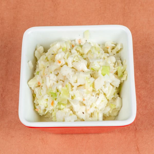 Creamy coleslaw with shredded cabbage, carrots, and green peppers in a white and red bowl.
