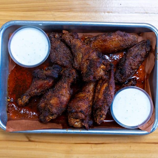 Crispy, dark brown chicken wings with two cups of ranch dressing in a metal tray.