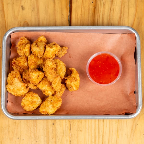 Crispy fried chicken nuggets and a small cup of red dipping sauce on a metal tray.