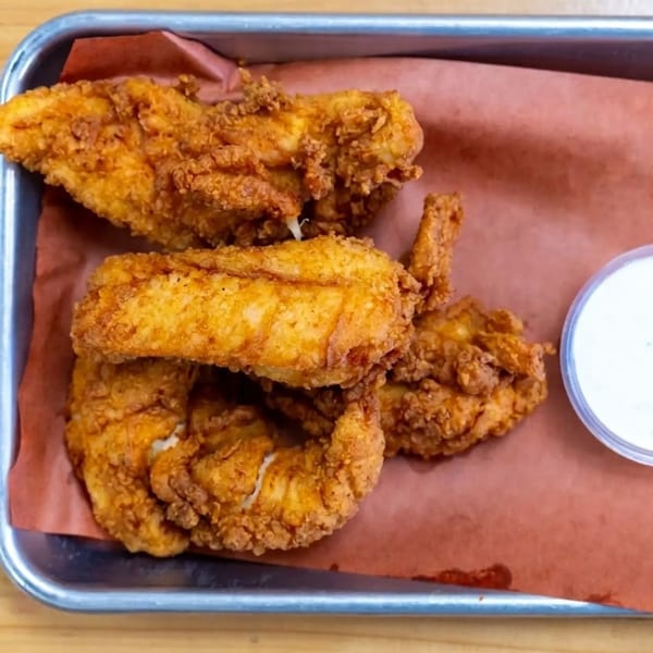Crispy fried chicken tenders and a side of white dipping sauce in a metal tray.