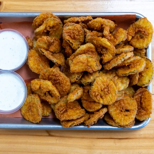 A metal tray filled with golden-brown fried pickles and two small cups of ranch dressing.