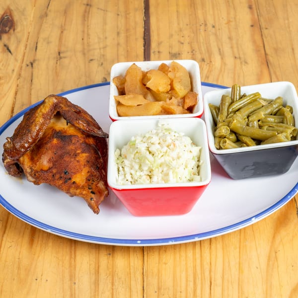 A plate of roasted chicken, coleslaw, green beans, and cinnamon apples on a wooden table.