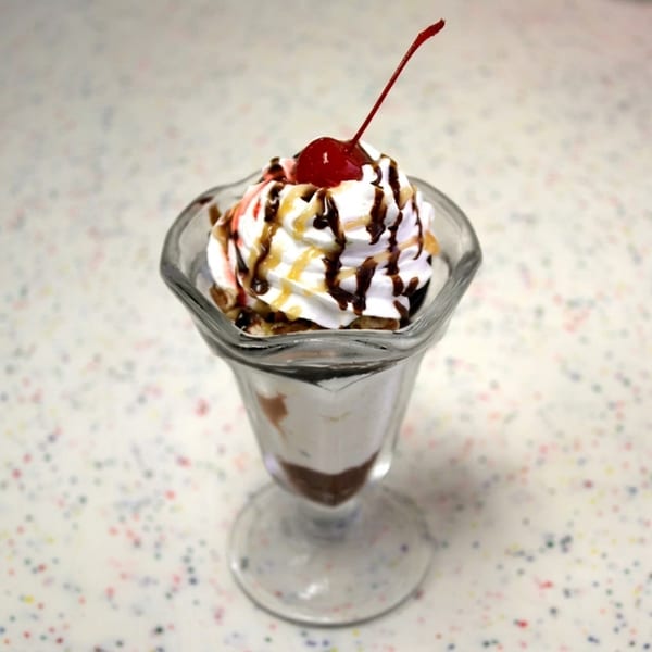 A classic ice cream sundae in a tall glass, topped with whipped cream, chocolate, caramel, and a cherry.