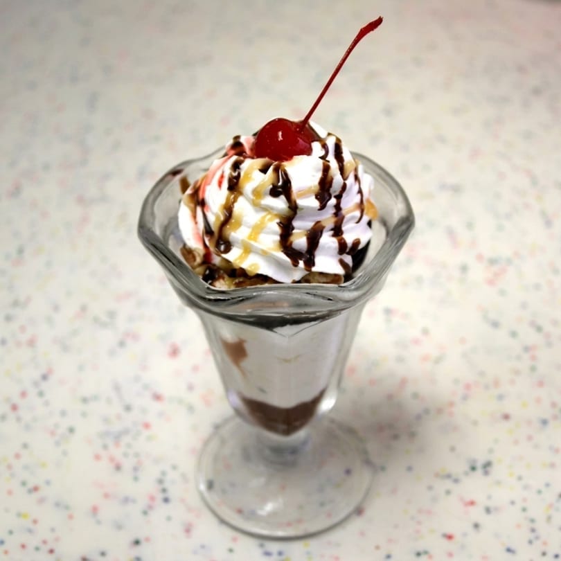 A classic ice cream sundae in a tall glass, topped with whipped cream, chocolate, caramel, and a cherry.