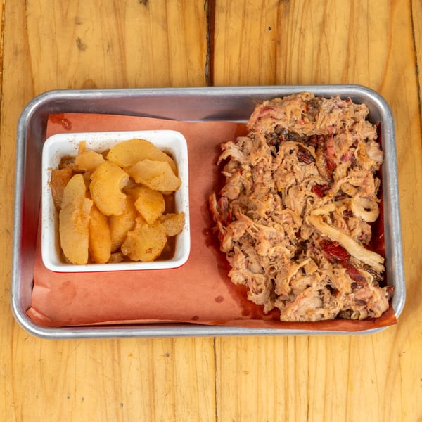 Pulled pork and a side of cinnamon apples on a metal tray with brown paper.