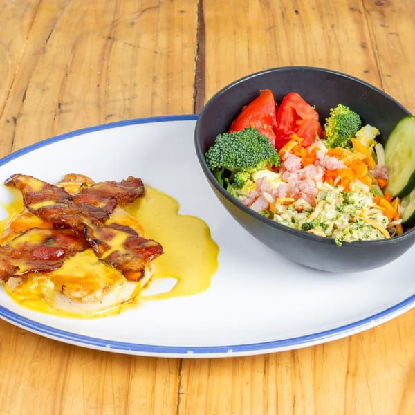 Chicken breast with melted cheese and bacon, alongside a salad with broccoli, tomatoes, and ham.