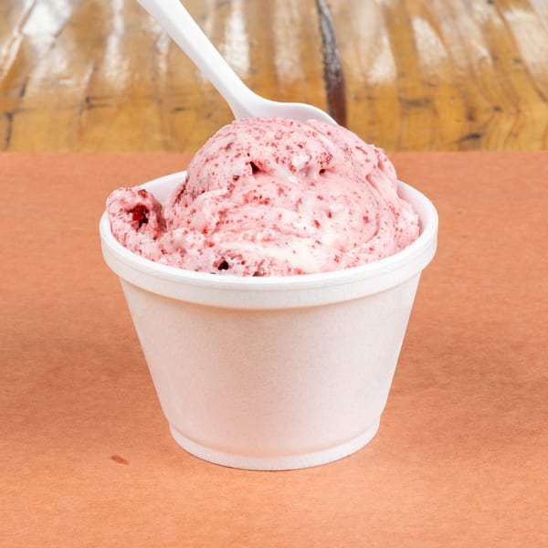 Strawberry ice cream in a white cup with a white spoon, on an orange surface.
