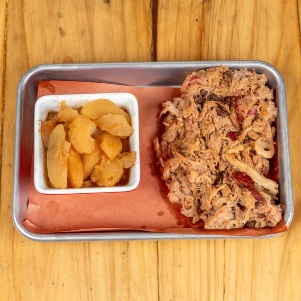 Pulled pork and a side of cinnamon-spiced apples on a metal tray with brown paper.