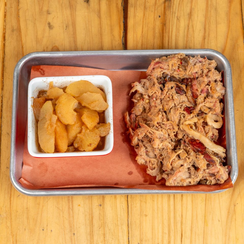 Pulled pork and a side of cinnamon-spiced apples on a metal tray with brown paper.
