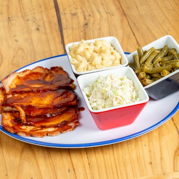 BBQ pork with mac and cheese, coleslaw, and green beans on a white plate.