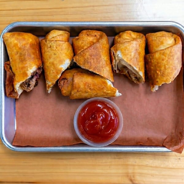 Six crispy, golden-brown egg rolls with meat filling, served on a tray with a side of ketchup.
