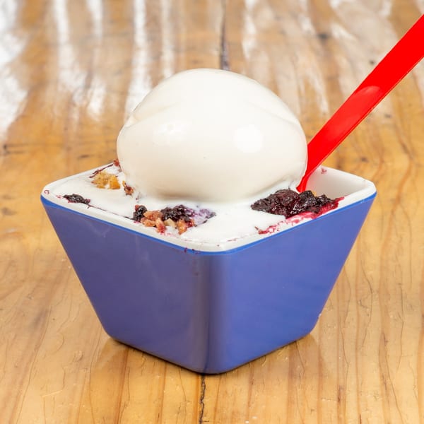 Blue bowl of berry crumble topped with a scoop of vanilla ice cream and a red spoon.